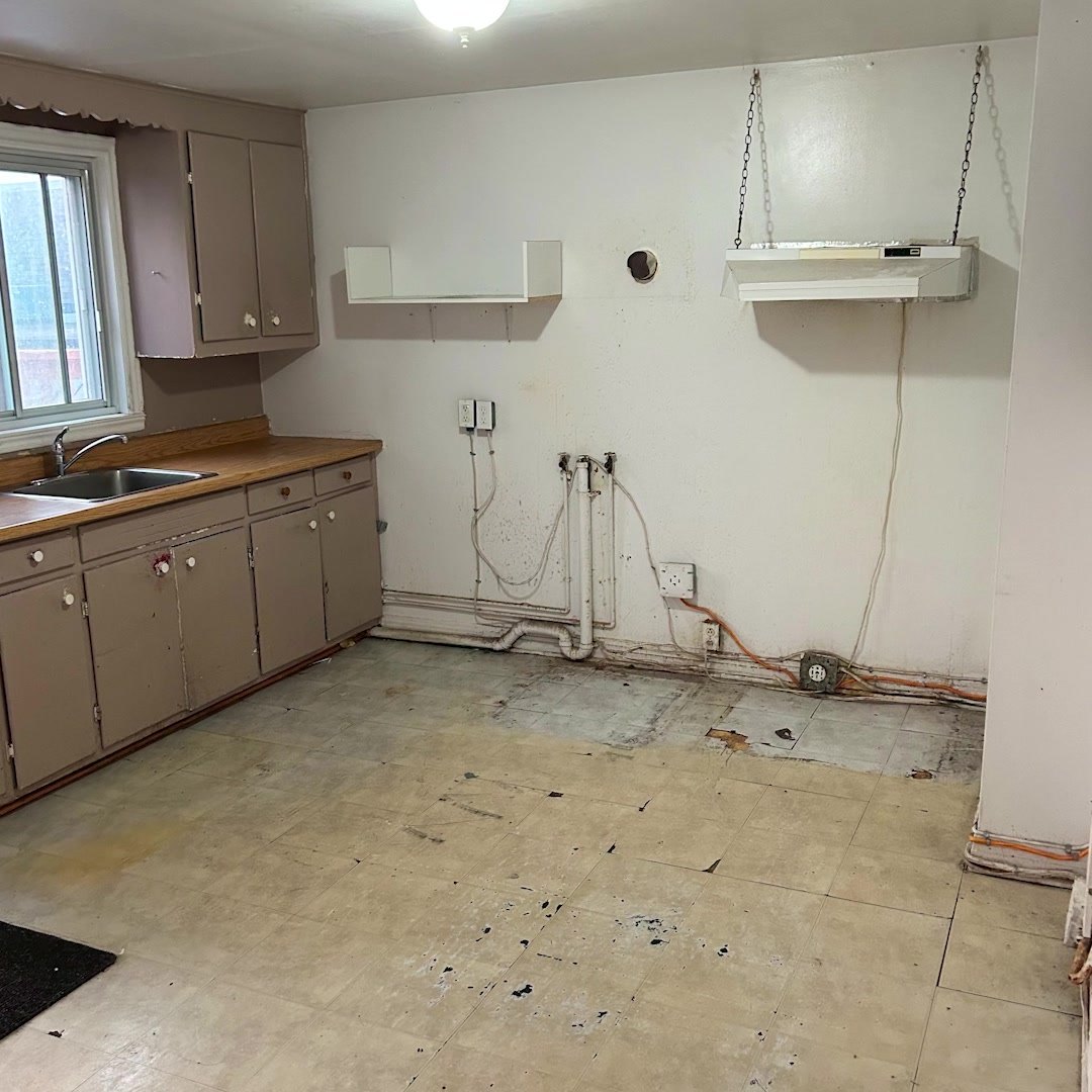 La cuisine avant les travaux : armoires d'origine, plancher abîmé et murs dégarnis