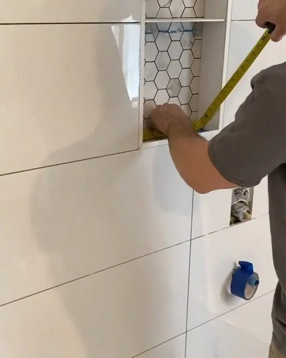 Pose de céramique murale : mesure au ruban près d'une niche en mosaïque