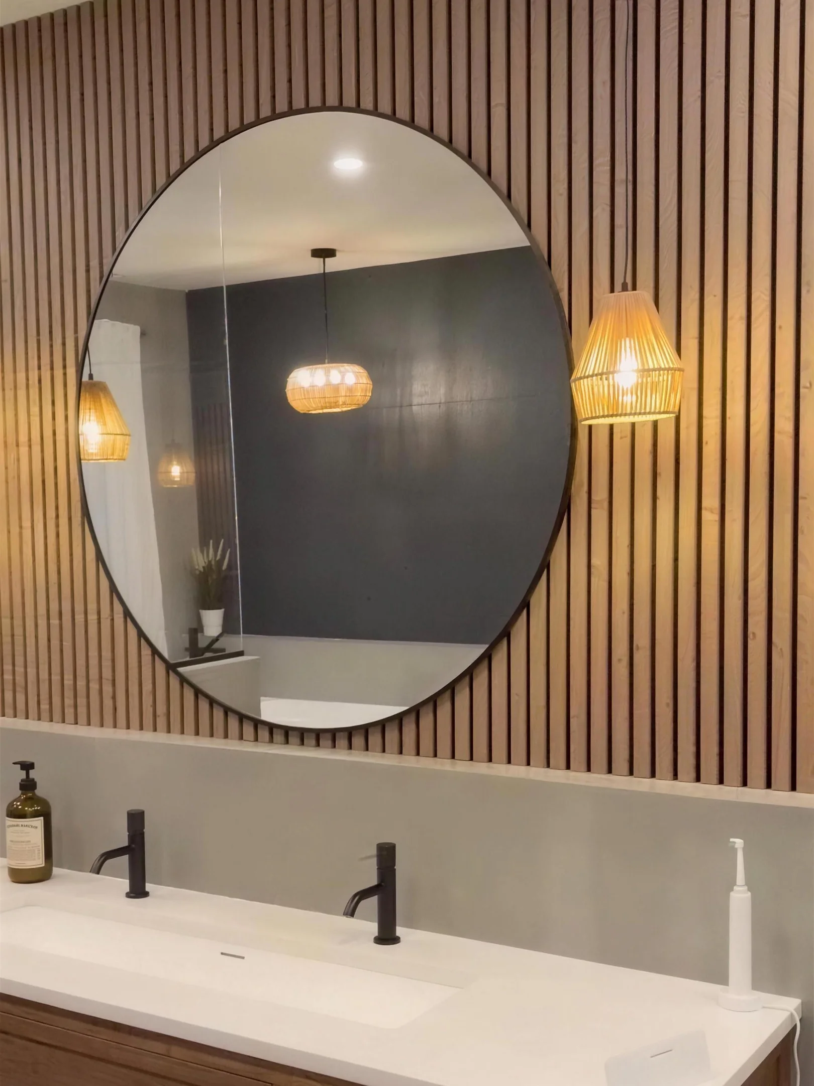 Salle de bain réalisée par Sévigny Boucher : mur de lattes de bois, miroir rond et vanité double