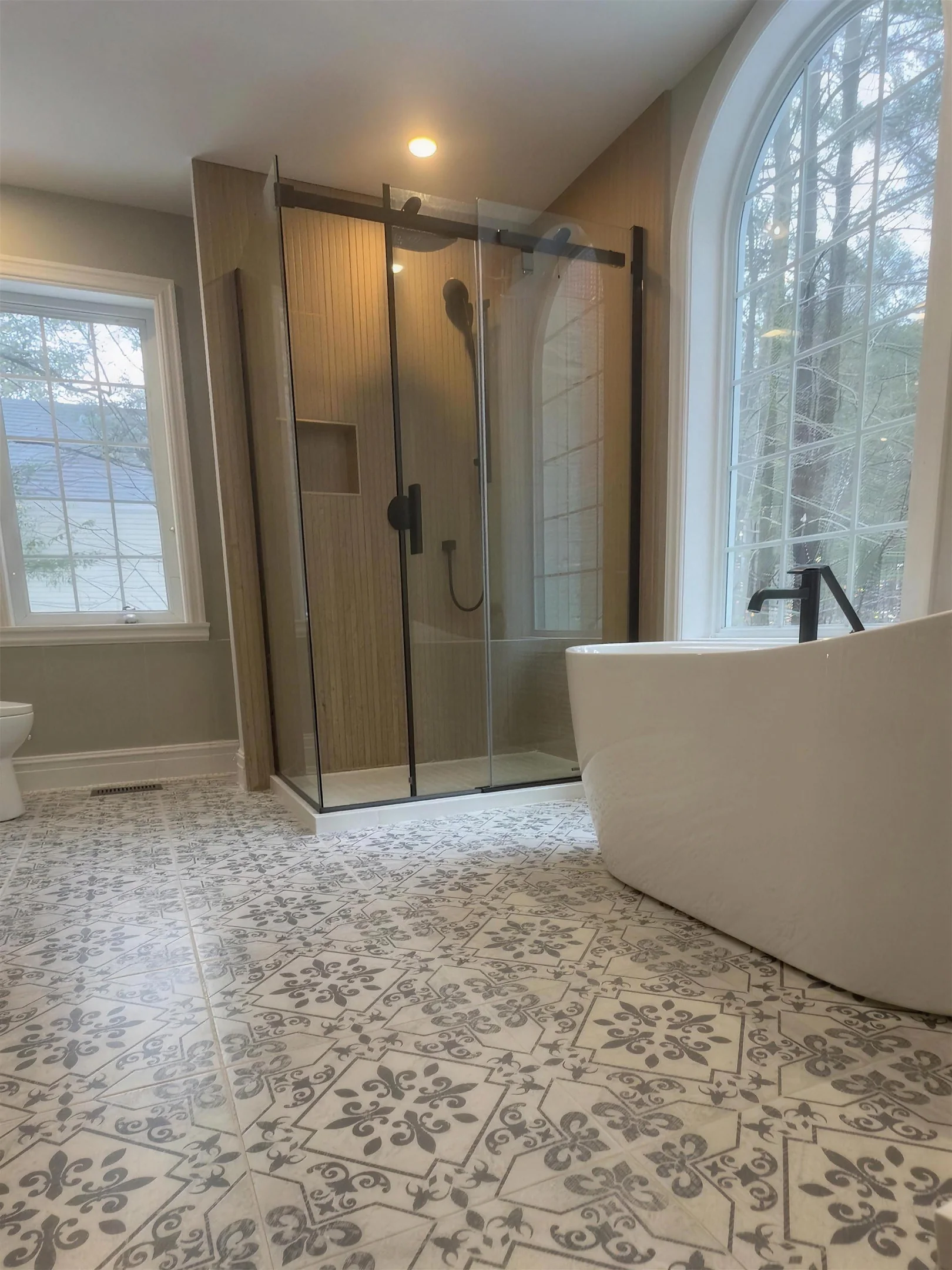 Salle de bain rénovée par Sévigny Boucher : bain autoportant devant une fenêtre en arche, douche vitrée et céramique à motifs