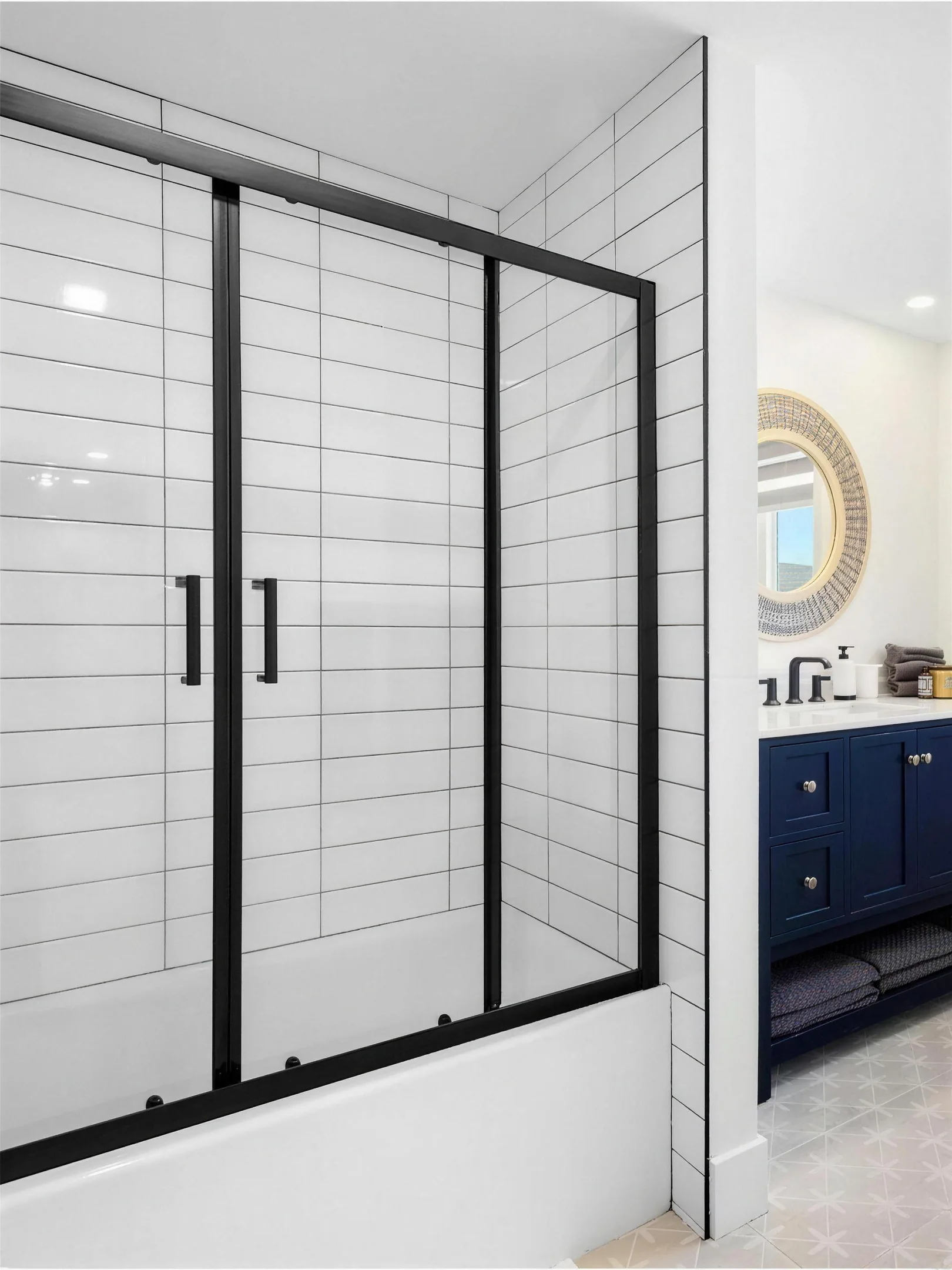 Salle de bain rénovée : douche vitrée aux profilés noirs, céramique blanche et vanité bleu marine